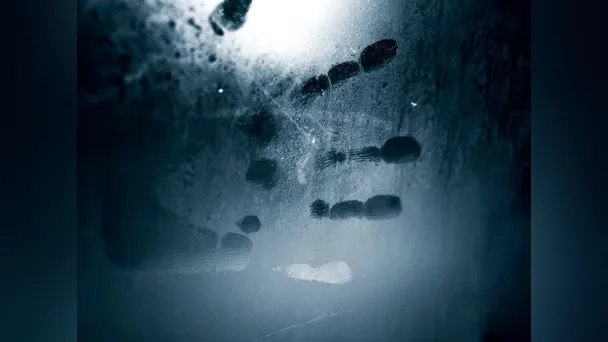 A shadowy handprint appears on fogged glass against a dark blue background.