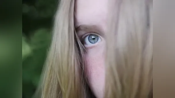 Close-up of a blue-eyed child peering through strands of blonde hair.